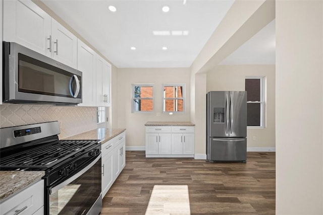 kitchen with light stone counters, dark wood-style floors, stainless steel appliances, white cabinetry, and backsplash