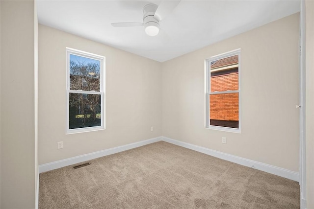 carpeted spare room with a ceiling fan, visible vents, and baseboards