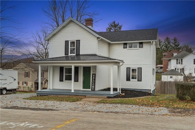 view of front of property featuring metal roof, fence, covered porch, and a chimney