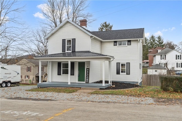 view of front of property featuring fence, a standing seam roof, covered porch, a chimney, and metal roof