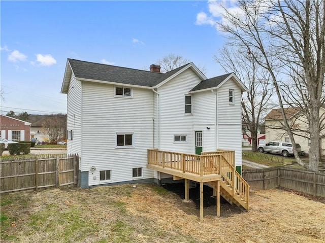 rear view of property featuring a fenced backyard, a chimney, roof with shingles, and a wooden deck