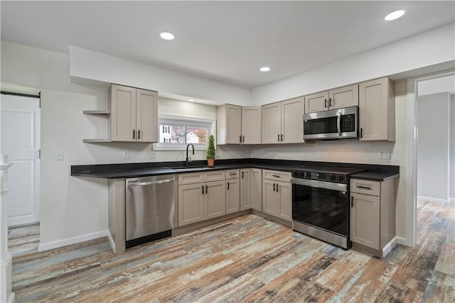 kitchen with dark countertops, open shelves, a sink, stainless steel appliances, and a barn door