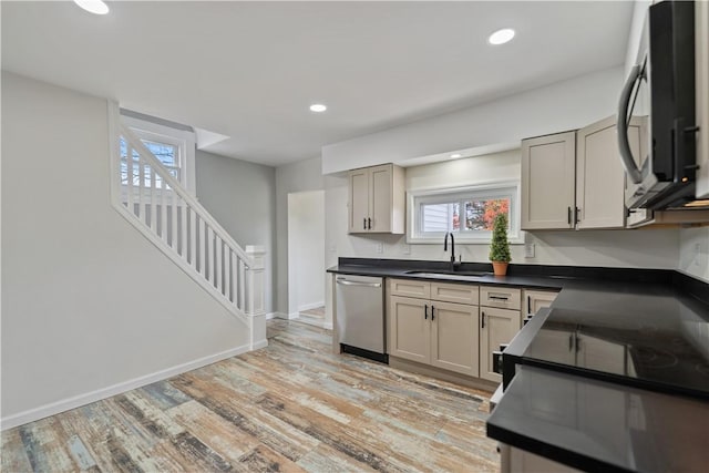 kitchen featuring dark countertops, black microwave, dishwasher, light wood-type flooring, and a sink