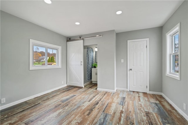 unfurnished bedroom with baseboards, a barn door, and wood finished floors