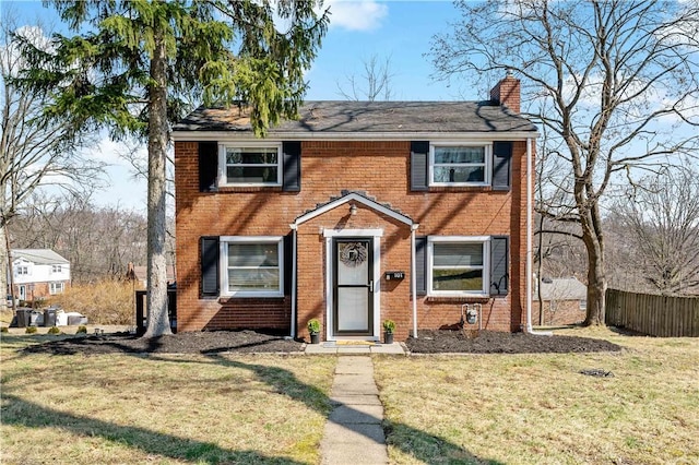 colonial house featuring brick siding, a chimney, a front yard, and fence