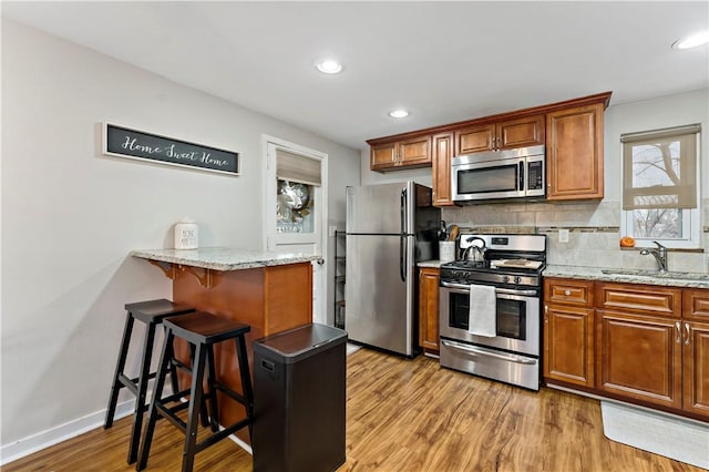 kitchen featuring a sink, a kitchen breakfast bar, backsplash, stainless steel appliances, and light wood-style floors