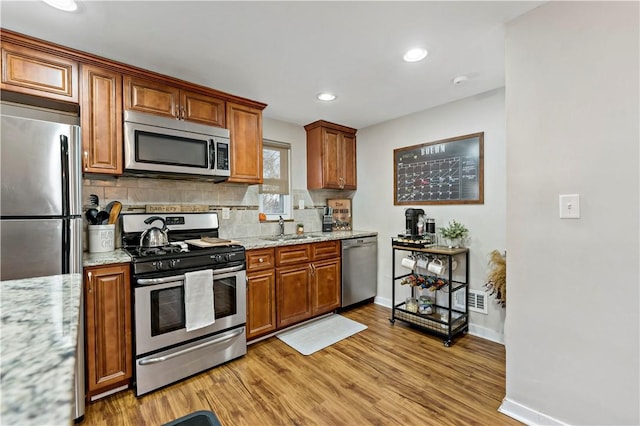 kitchen featuring a sink, stainless steel appliances, light wood-style floors, and backsplash