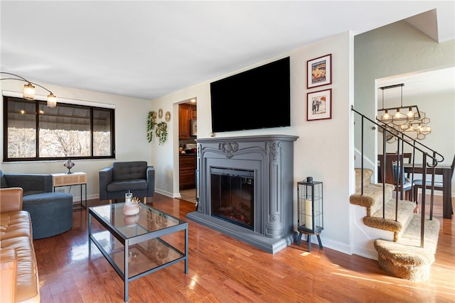 living area featuring wood finished floors, baseboards, stairs, a glass covered fireplace, and a notable chandelier