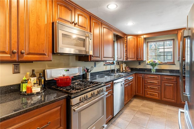 kitchen featuring brown cabinetry, dark stone counters, recessed lighting, a sink, and stainless steel appliances