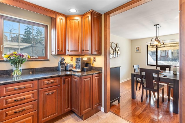 kitchen featuring dark stone counters, baseboards, brown cabinets, and hanging light fixtures