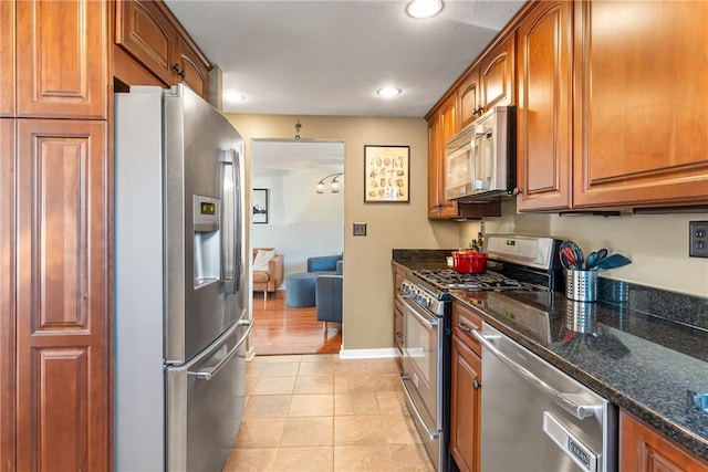 kitchen featuring light tile patterned floors, appliances with stainless steel finishes, dark stone counters, and brown cabinetry