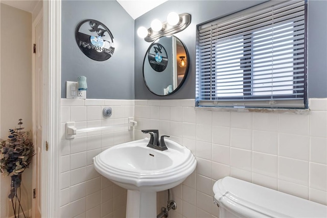 half bathroom with wainscoting, toilet, tile walls, and a sink