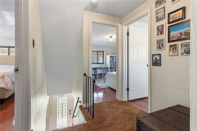 hall with an upstairs landing, carpet flooring, and wood finished floors