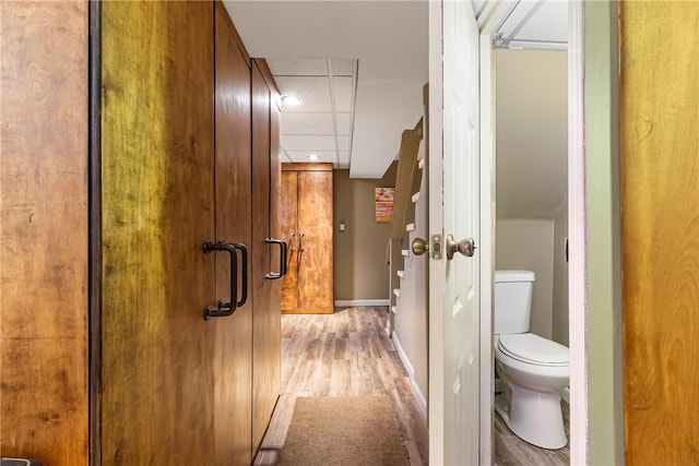 hallway with a paneled ceiling, light wood-type flooring, and baseboards