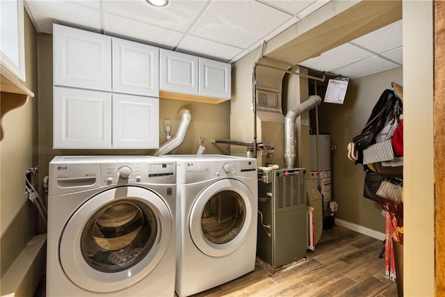 clothes washing area featuring baseboards, washing machine and clothes dryer, cabinet space, a heating unit, and light wood-type flooring