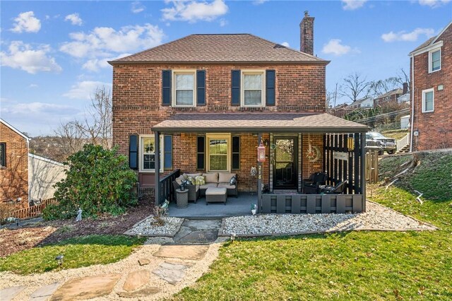 back of property with an outdoor living space, a porch, a yard, brick siding, and a chimney