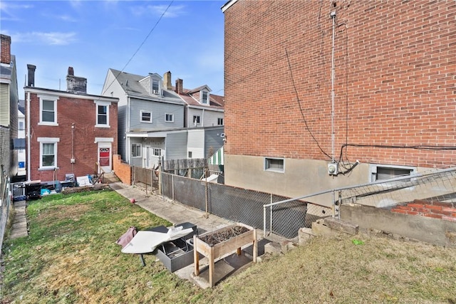 back of house with entry steps, fence, a yard, a vegetable garden, and brick siding