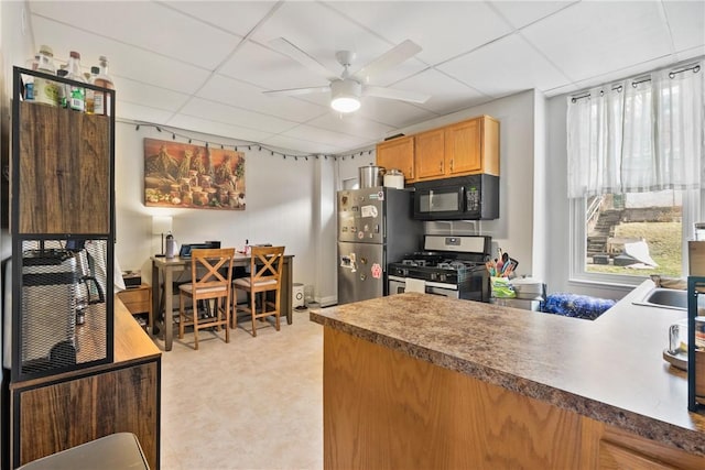 kitchen with a peninsula, a ceiling fan, appliances with stainless steel finishes, and a paneled ceiling