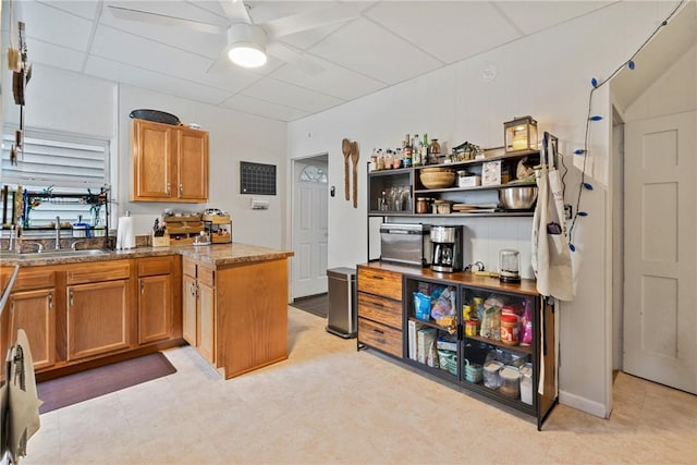 kitchen with a sink, brown cabinets, a peninsula, and a ceiling fan