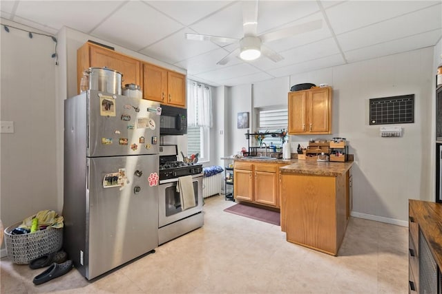 kitchen with a drop ceiling, appliances with stainless steel finishes, brown cabinetry, baseboards, and ceiling fan