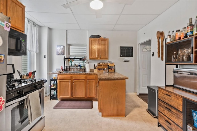 kitchen featuring black microwave, ceiling fan, a drop ceiling, stainless steel gas range, and a sink