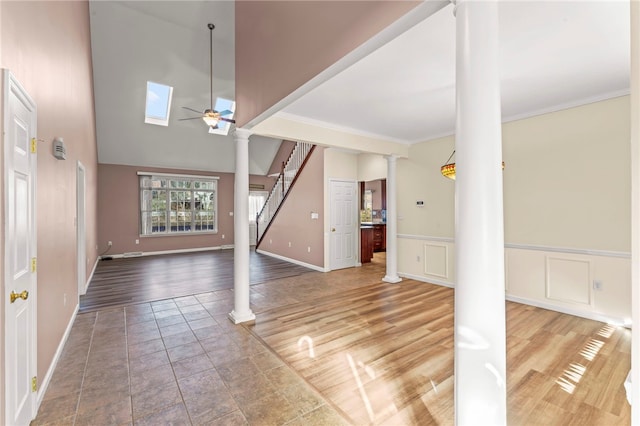 entryway featuring a ceiling fan, crown molding, light wood finished floors, wainscoting, and ornate columns