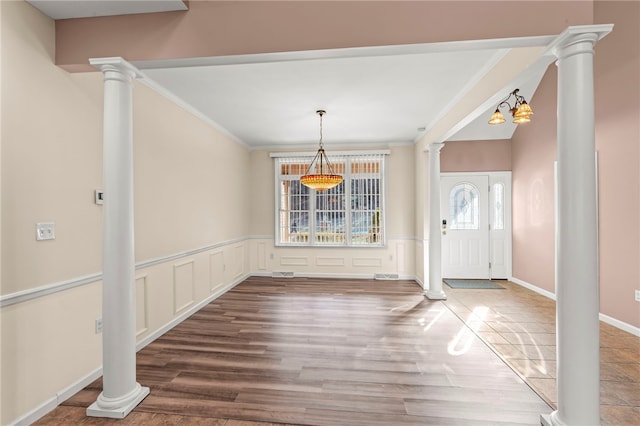 foyer with decorative columns, wood finished floors, a wainscoted wall, and crown molding