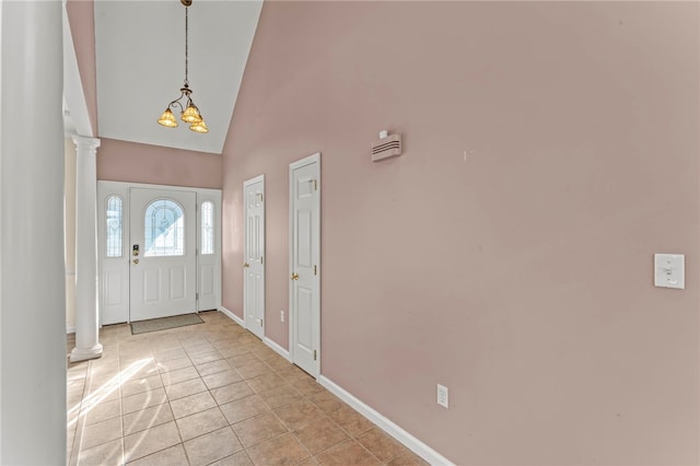 entryway featuring baseboards, ornate columns, high vaulted ceiling, light tile patterned flooring, and a chandelier