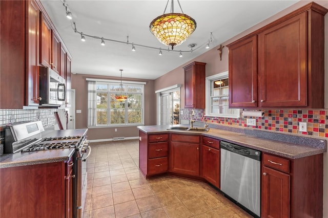 kitchen featuring dark countertops, pendant lighting, decorative backsplash, appliances with stainless steel finishes, and a sink