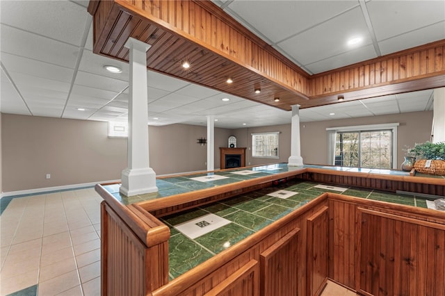 bar featuring a drop ceiling, decorative columns, a fireplace, and light tile patterned floors