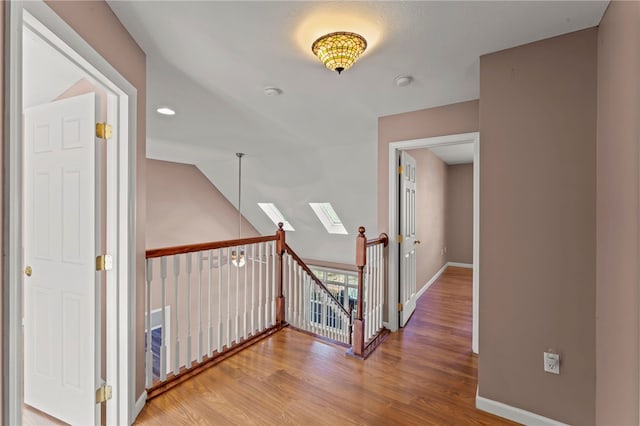 hall with an upstairs landing, vaulted ceiling with skylight, baseboards, and wood finished floors