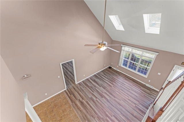 unfurnished living room with ceiling fan, baseboards, light wood-style flooring, a skylight, and high vaulted ceiling