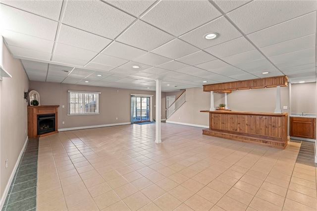 below grade area featuring a fireplace, light tile patterned flooring, a paneled ceiling, and baseboards