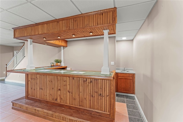 interior space with tile patterned floors, a paneled ceiling, baseboards, and a sink