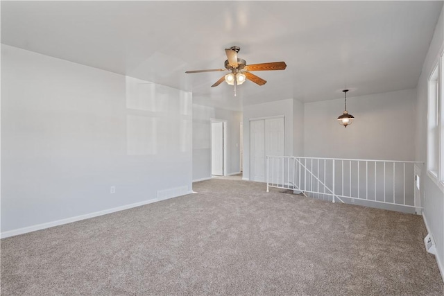 carpeted spare room with visible vents, baseboards, and ceiling fan