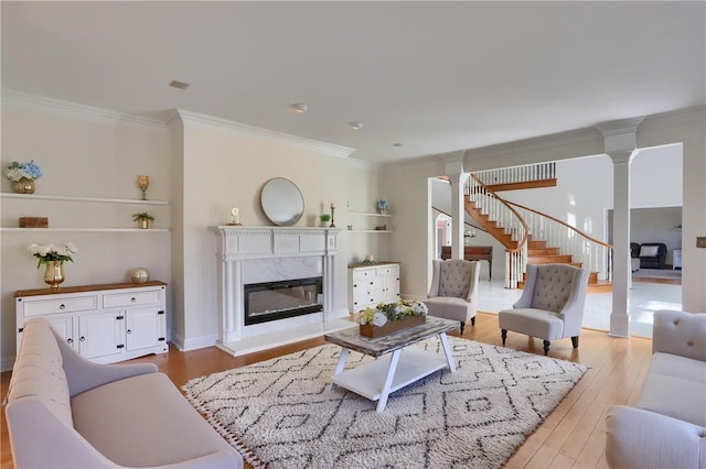 living area with a high end fireplace, crown molding, stairway, wood finished floors, and ornate columns