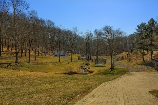 view of community with a rural view, fence, dirt driveway, a lawn, and an outbuilding