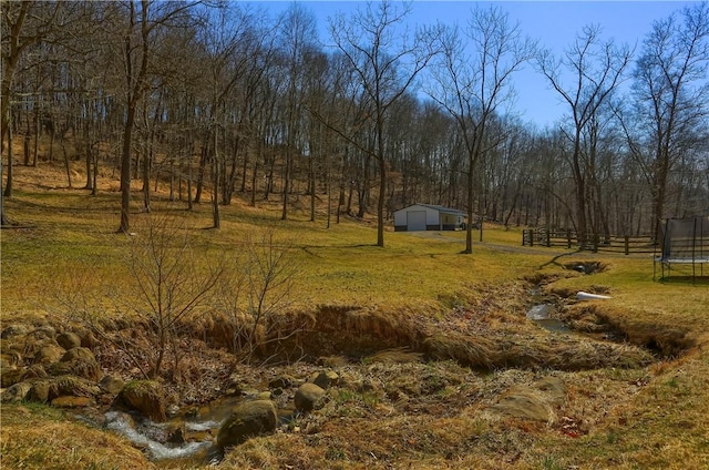 view of yard with a wooded view, a trampoline, fence, a garage, and an outdoor structure