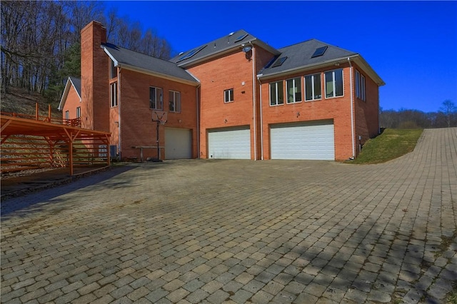 back of property featuring brick siding, an attached garage, a chimney, and decorative driveway