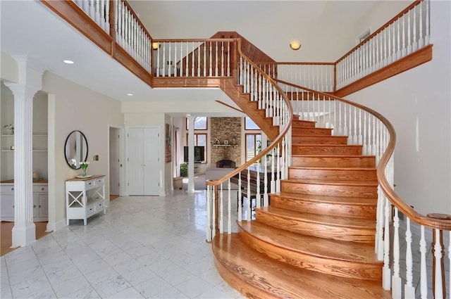 stairs featuring decorative columns, a stone fireplace, recessed lighting, a towering ceiling, and marble finish floor