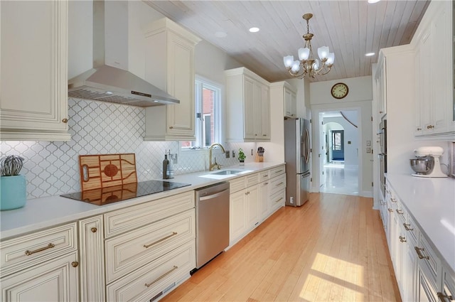 kitchen featuring wall chimney range hood, light countertops, an inviting chandelier, stainless steel appliances, and a sink