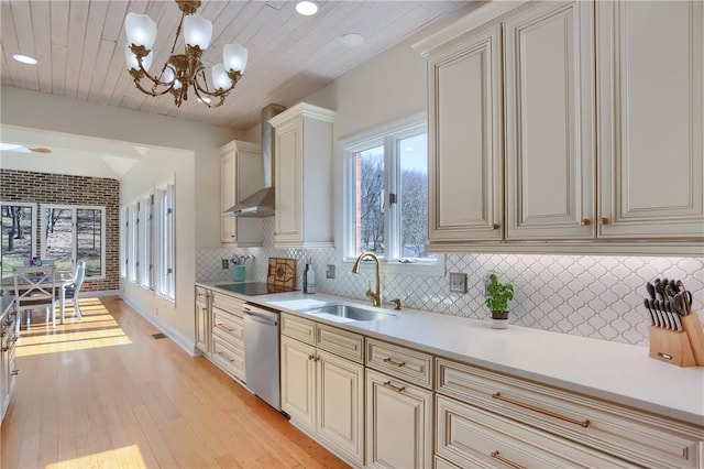 kitchen featuring wall chimney range hood, dishwasher, light countertops, cream cabinets, and a sink