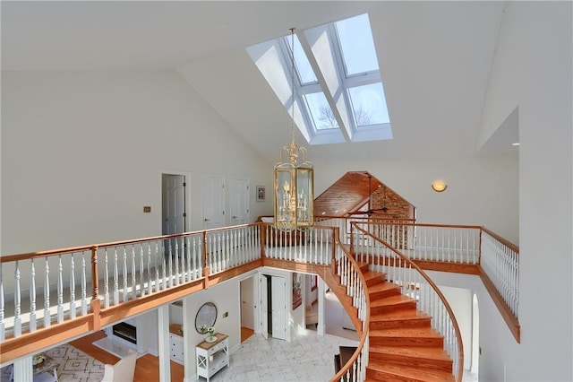 staircase featuring a chandelier, high vaulted ceiling, and a skylight