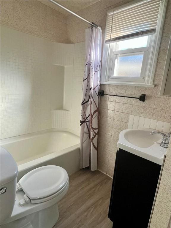 bathroom with toilet, wood finished floors, tile walls, shower / tub combo, and vanity