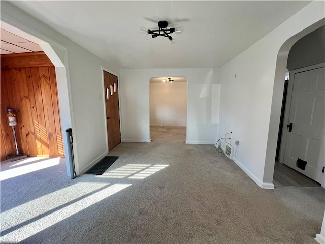 carpeted spare room featuring arched walkways and baseboards