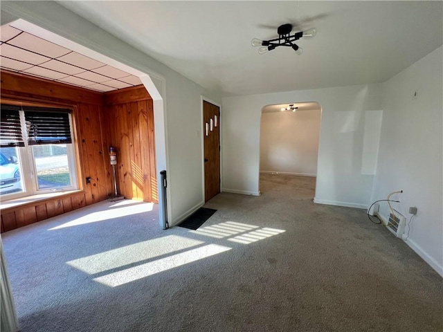 unfurnished room with baseboards, arched walkways, carpet, and wooden walls