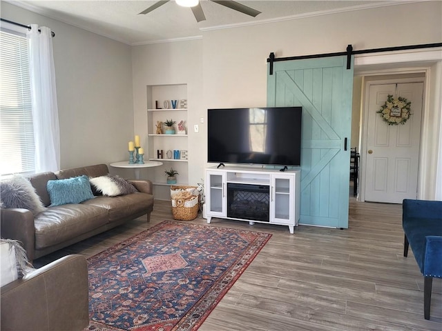 living room with a ceiling fan, built in features, wood finished floors, a barn door, and crown molding