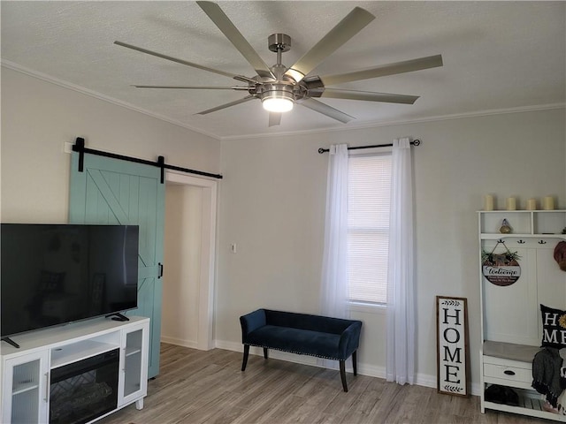 living area featuring light wood-type flooring, a ceiling fan, a barn door, crown molding, and baseboards