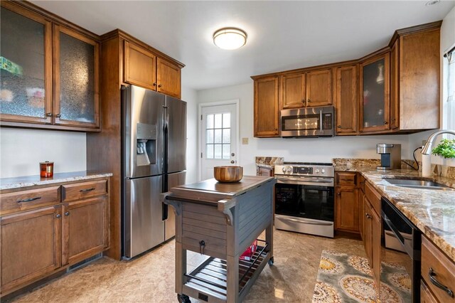 kitchen featuring a sink, light stone counters, brown cabinets, and stainless steel appliances