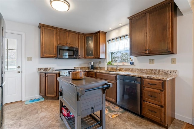 kitchen with stainless steel microwave, light stone counters, dishwashing machine, brown cabinetry, and a sink